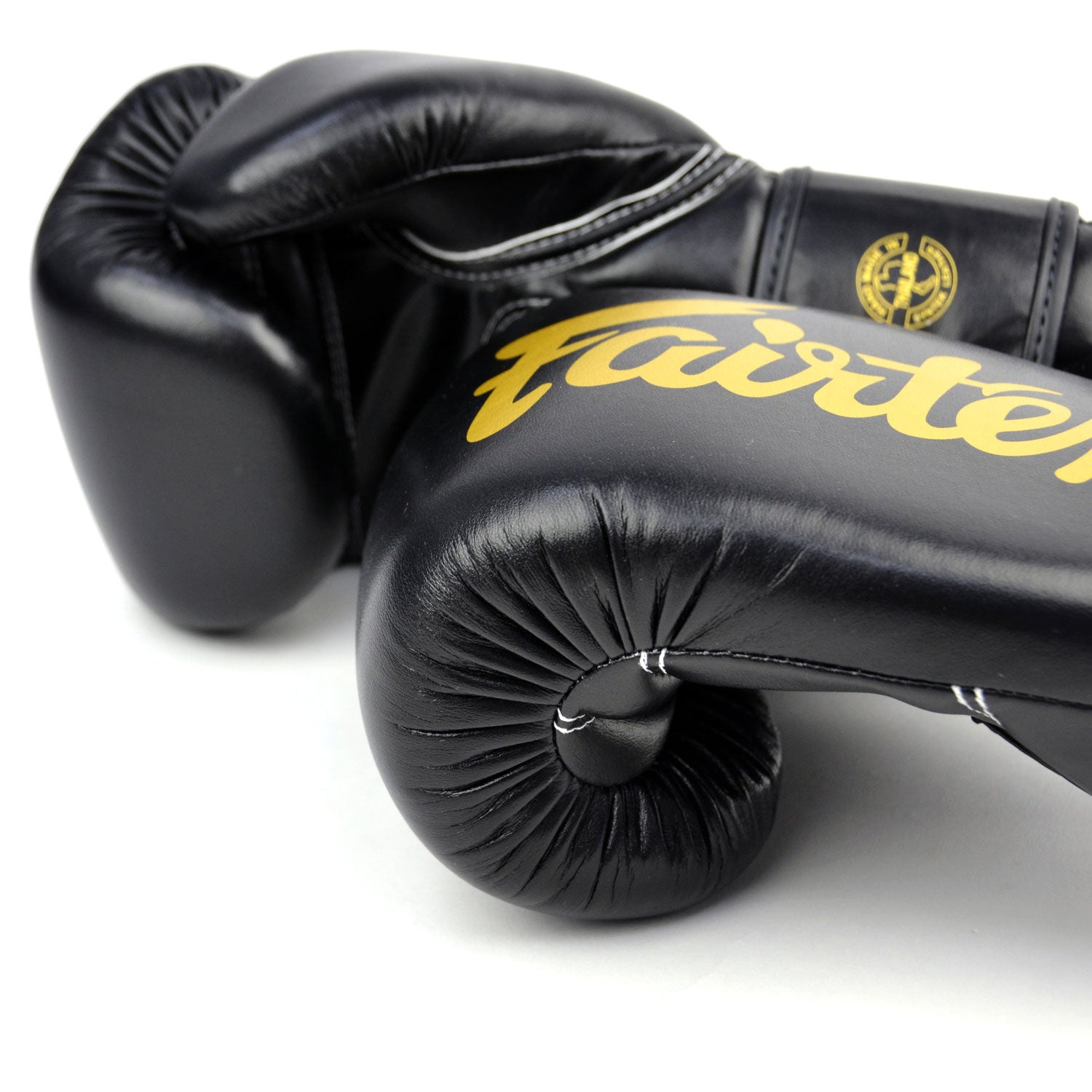 Black boxing gloves with gold 'Fairtex' branding on a white background