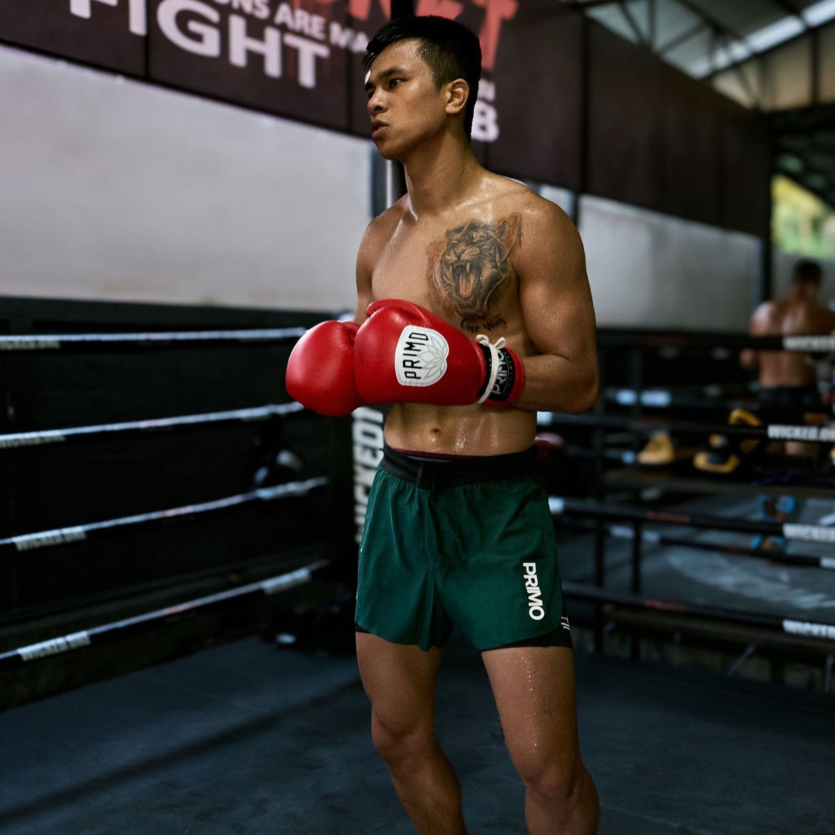 Boxer in red gloves and green shorts standing in a boxing ring.
