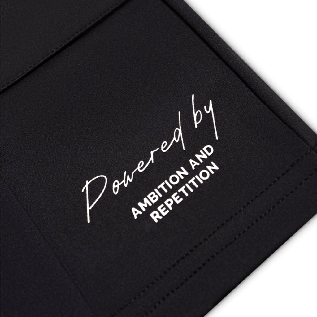 Black surface with white text 'Powered by Ambition and Repetition'