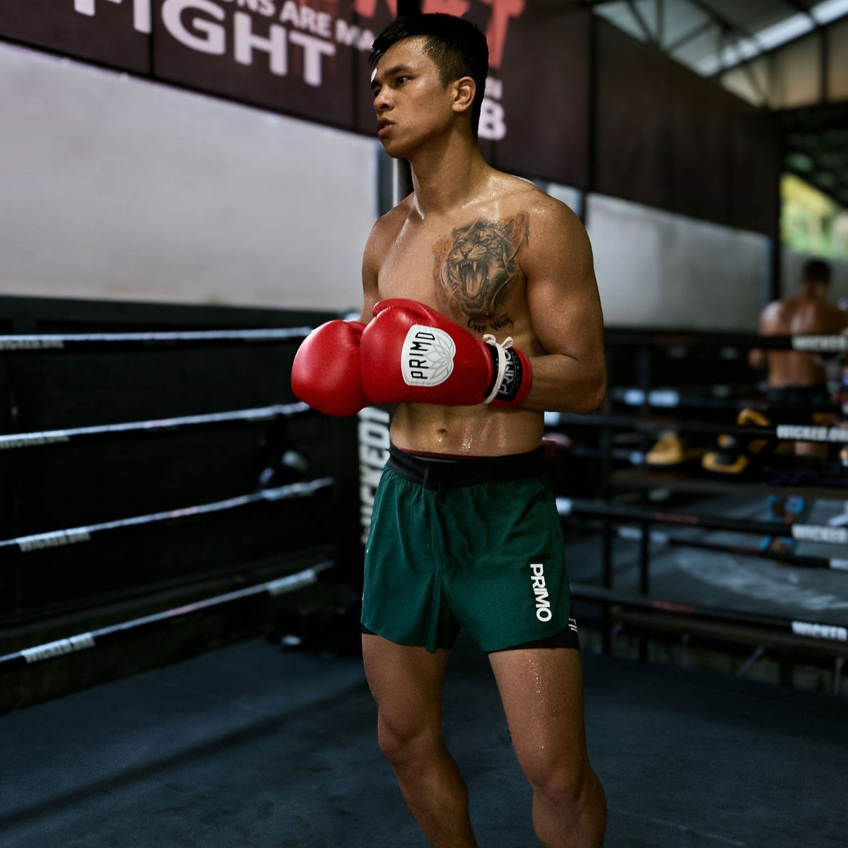 Boxer in green shorts and red gloves standing in a boxing ring.