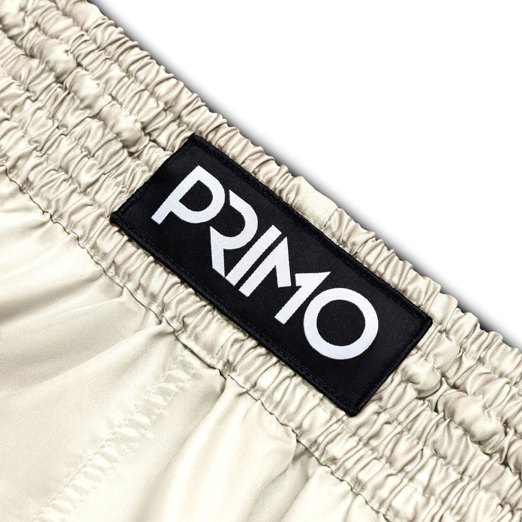 Beige shorts with a black 'Primo' logo patch on a white background