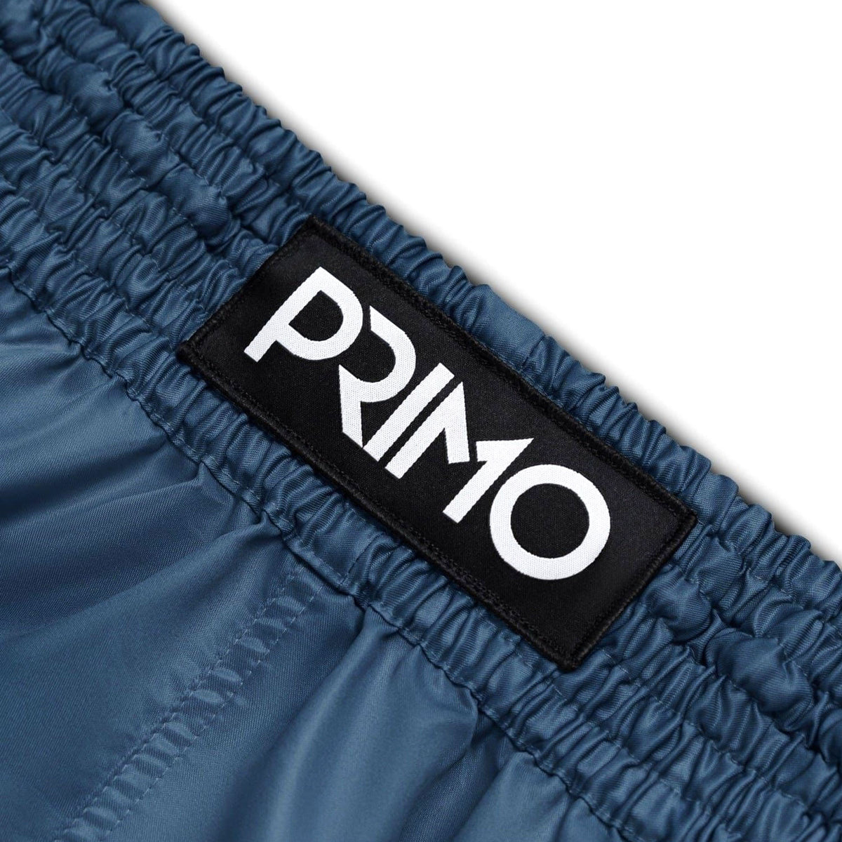 Close-up of blue shorts with a 'Primo' logo patch on a white background