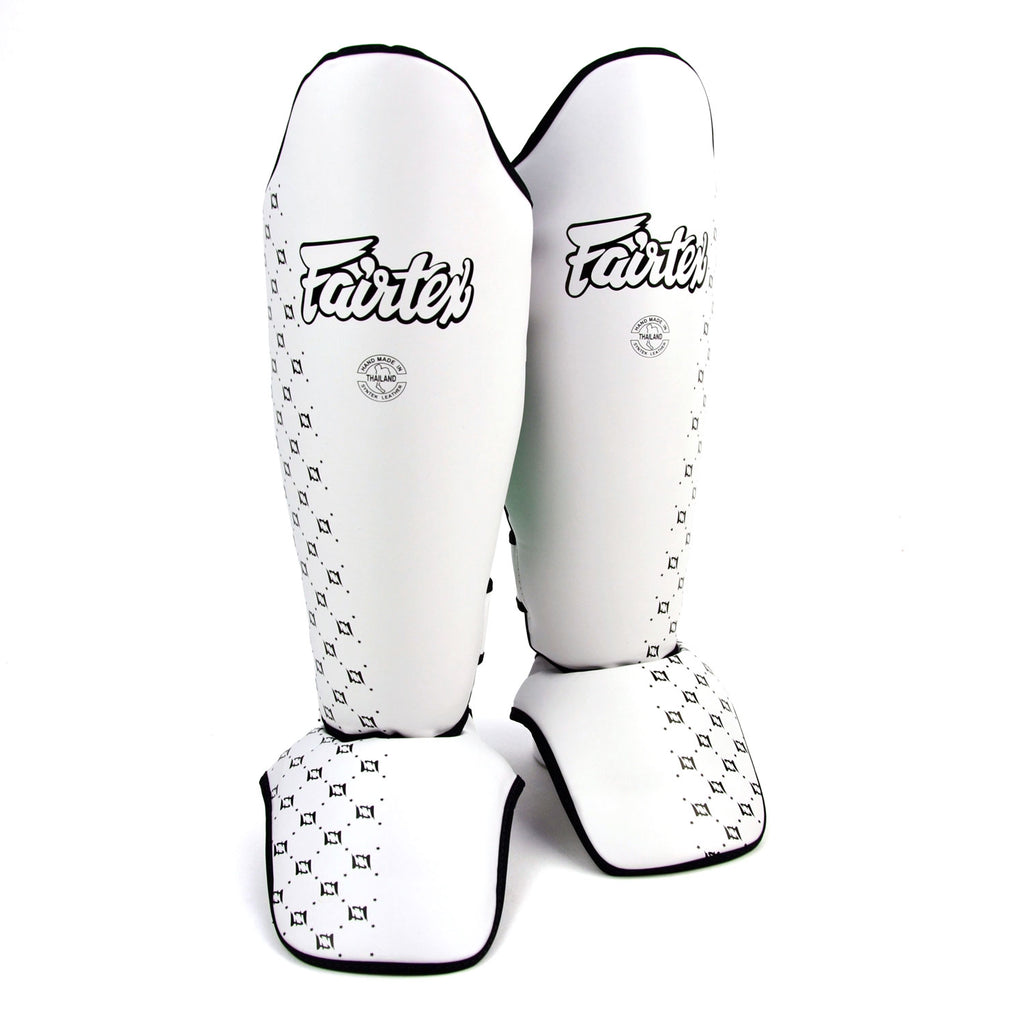 Pair of white shin guards with black patterns and 'Fairtex' branding on a white background